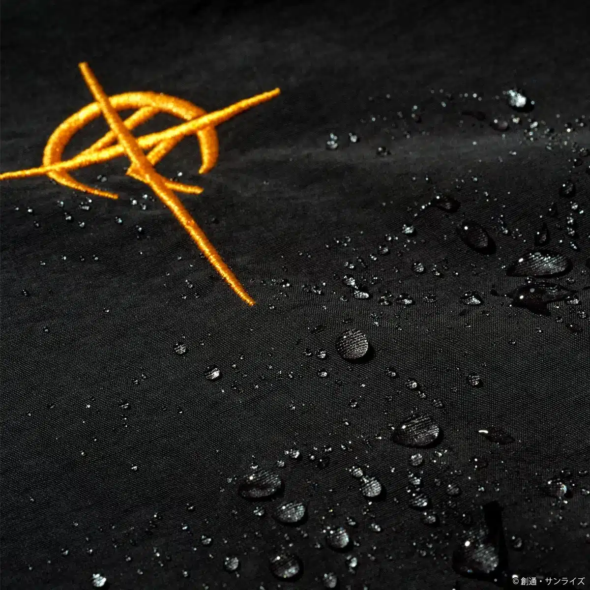黒い生地にオレンジ色の複雑な刺繍が施されており、表面には多数の水滴が付着しています。