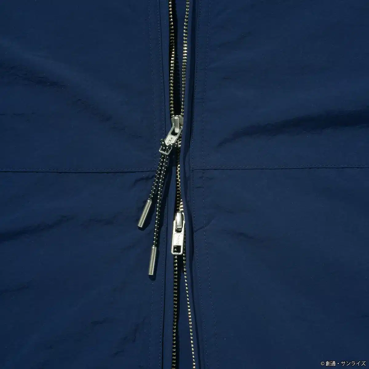 ネイビーの生地に施されたメタリックなジッパーとドローコードのクローズアップ画像です。
