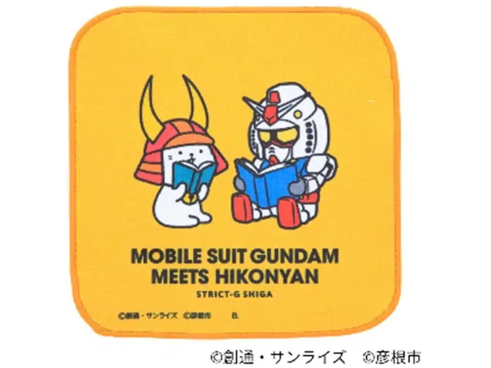 黄色い背景に、ガンダムとひこにゃんが本を読む姿が描かれた可愛らしいイラストのグッズです。「MOBILE SUIT GUNDAM MEETS HIKONYAN STRICT-G SHIGA」の文字があり、両者のコラボレーション商品を示しています。