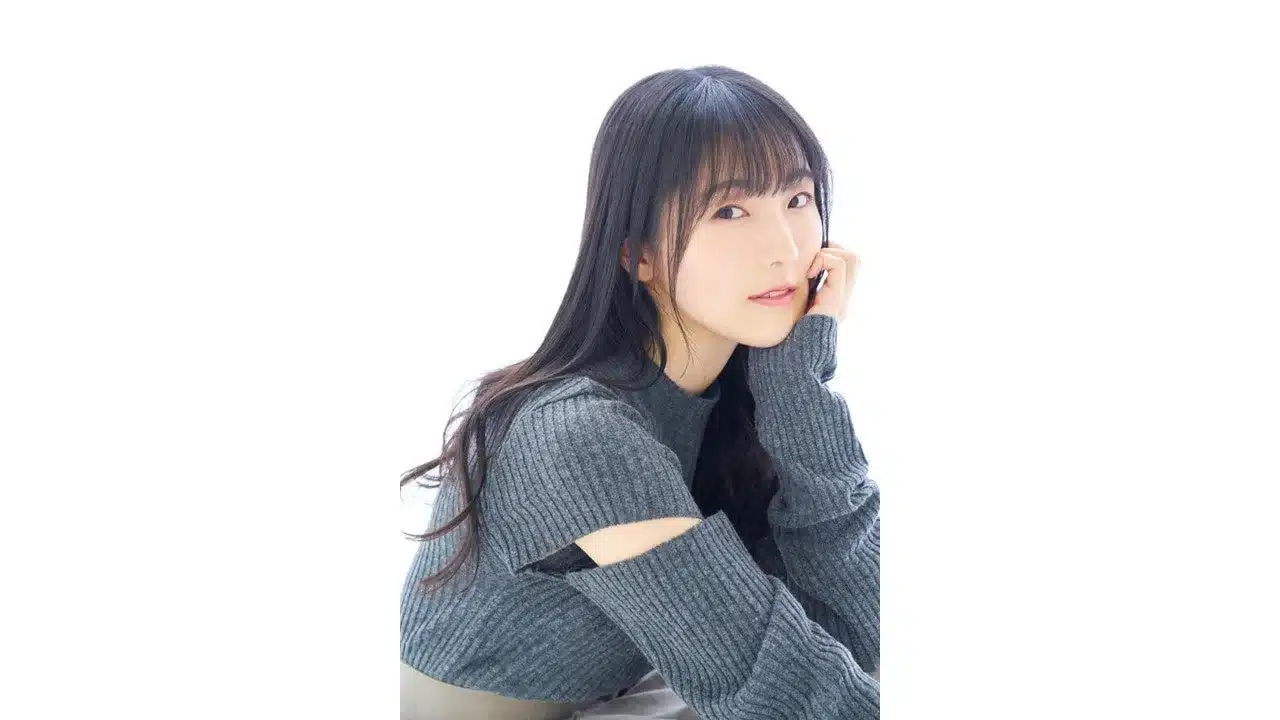 白い背景の前で、グレーのリブニットを着た若い女性が優しく微笑んでいます。